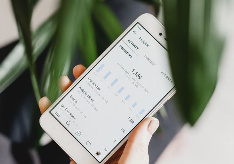 Mão com celular na página de métricas do Instagram